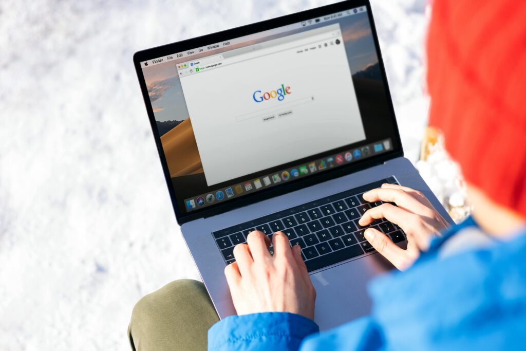 Individual typing on a laptop outdoors with snow, accessing the internet.